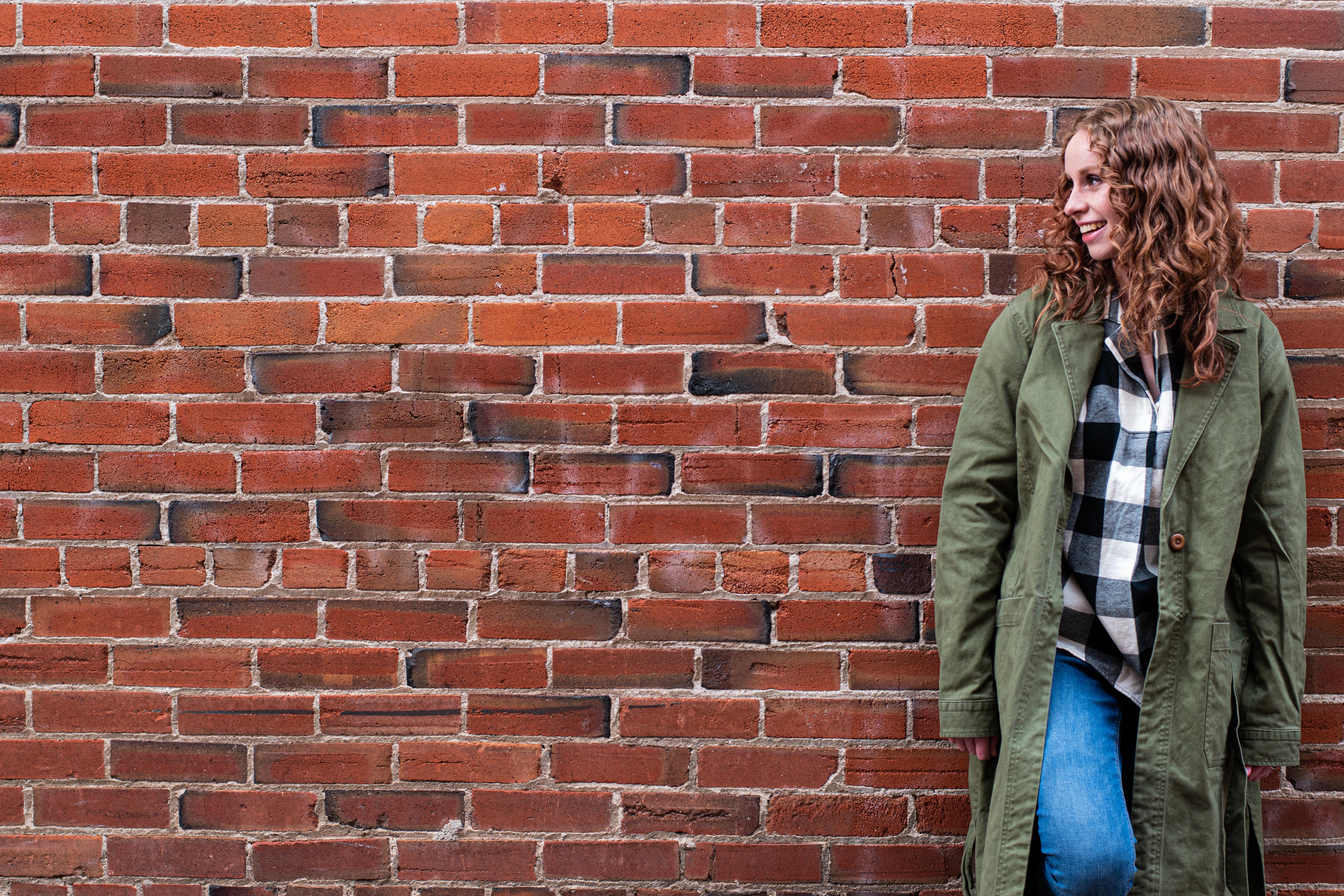Small business content writer looking to the left and smiling in front of brick wall.